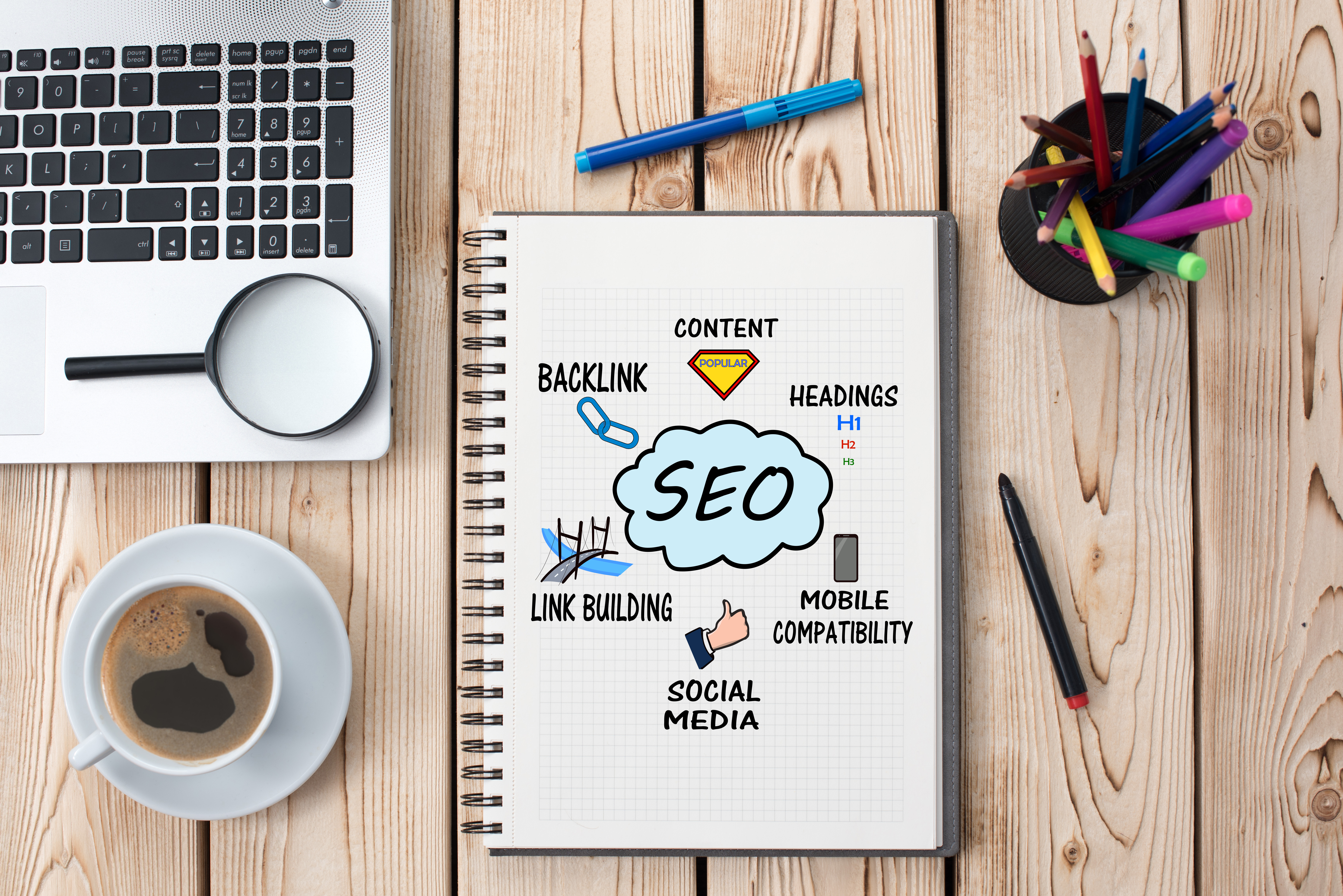 Overhead view of a notebook displaying search engine optimization concepts on a wooden tabletop with other office supplies.