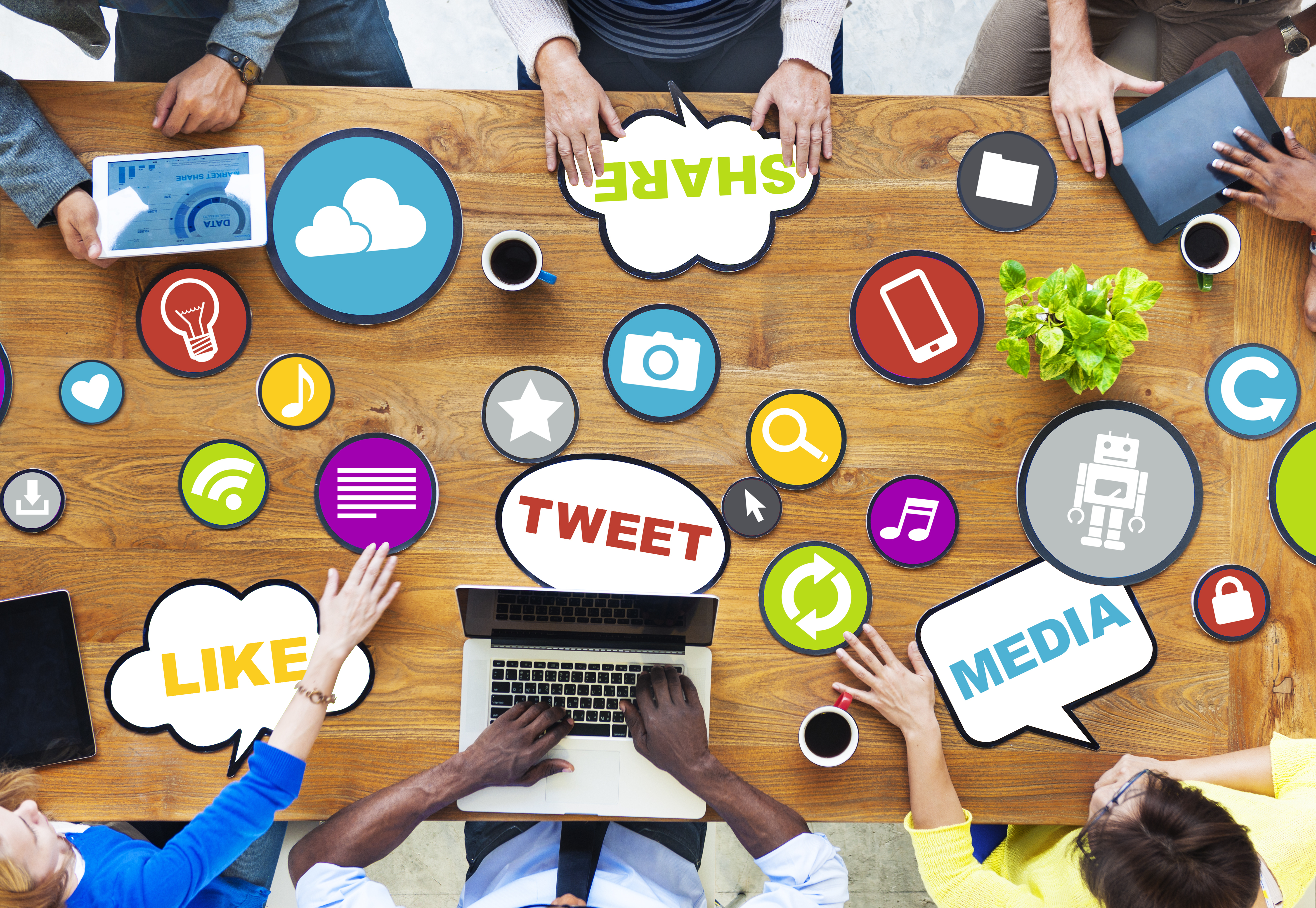 Overhead view of seven people sitting around a long table cluttered with social media key words and icons.